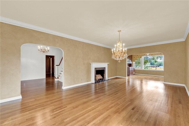 unfurnished living room with a chandelier, arched walkways, light wood-style floors, and a high end fireplace