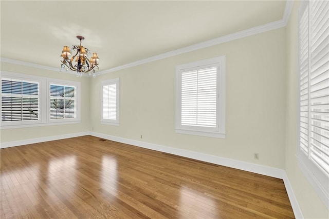 spare room featuring an inviting chandelier, crown molding, wood finished floors, and baseboards