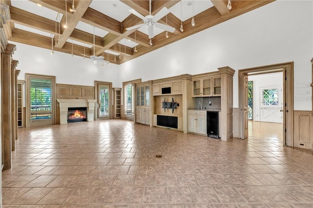 unfurnished living room featuring beverage cooler, beamed ceiling, a glass covered fireplace, coffered ceiling, and a ceiling fan