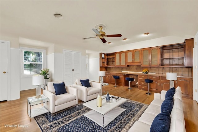 living room with light wood-type flooring, built in desk, and ceiling fan