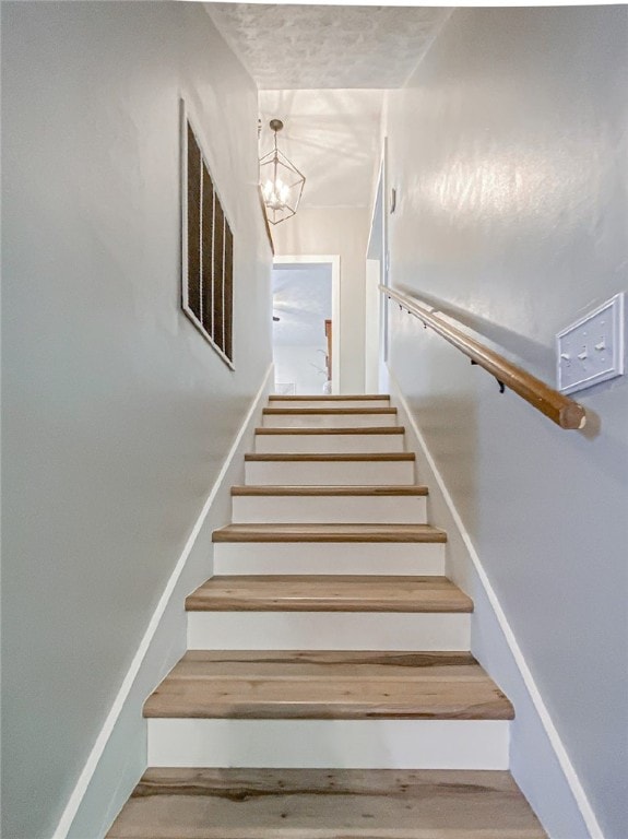 staircase with wood-type flooring and a chandelier