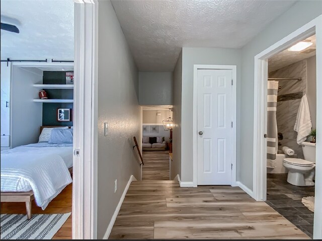 bedroom with a barn door, hardwood / wood-style floors, a textured ceiling, and ensuite bath