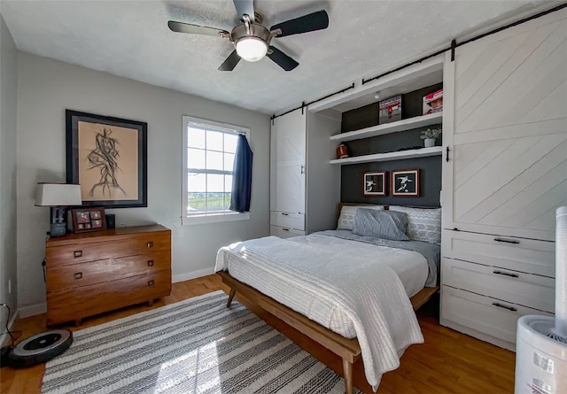 bedroom with a barn door, ceiling fan, and hardwood / wood-style flooring