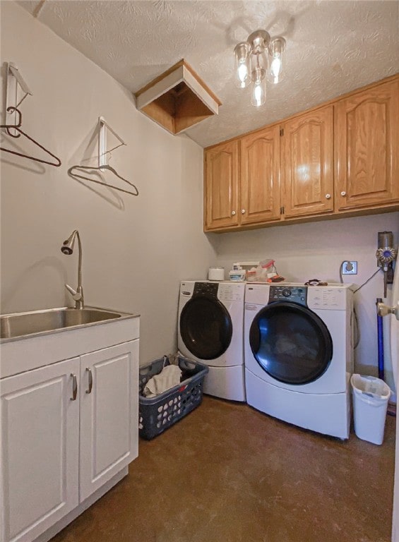 washroom with a textured ceiling, cabinets, washer and clothes dryer, and sink