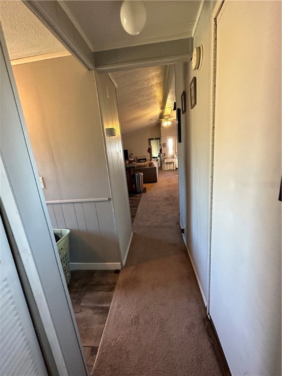 hallway with a textured ceiling, dark colored carpet, and vaulted ceiling with beams