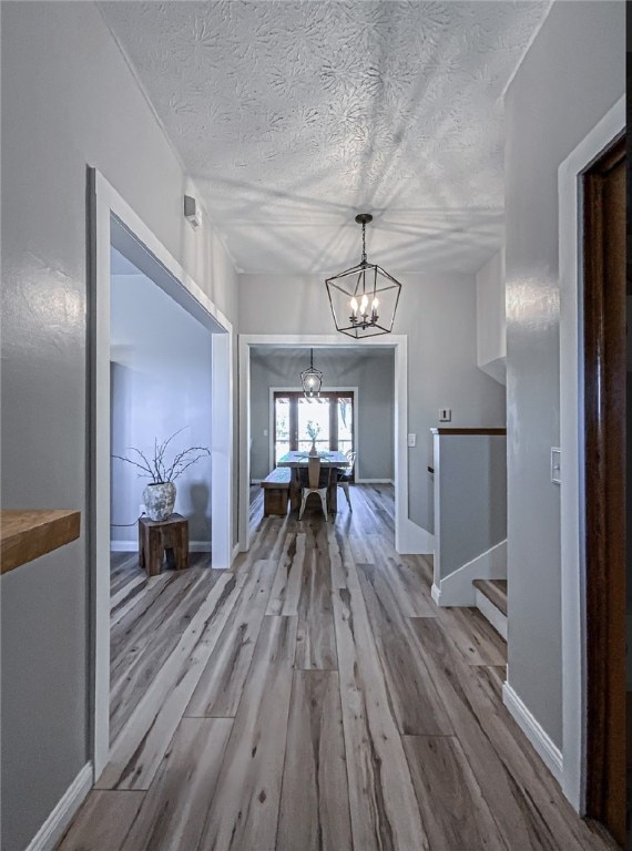 hallway featuring wood-type flooring, a notable chandelier, and a textured ceiling