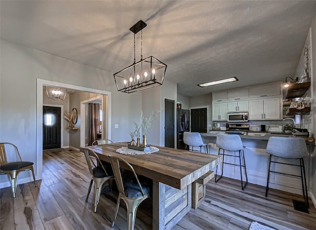 dining space featuring a textured ceiling, a notable chandelier, hardwood / wood-style floors, and sink