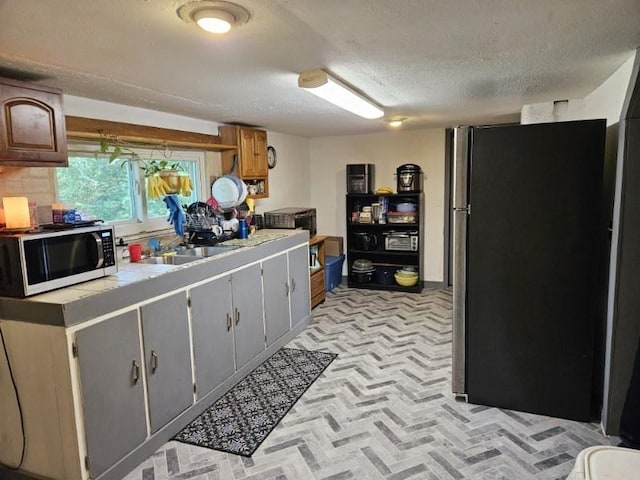 kitchen with a textured ceiling, decorative backsplash, stainless steel fridge, and sink