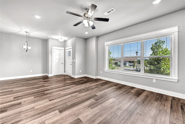 empty room featuring ceiling fan with notable chandelier, wood-type flooring, and a healthy amount of sunlight