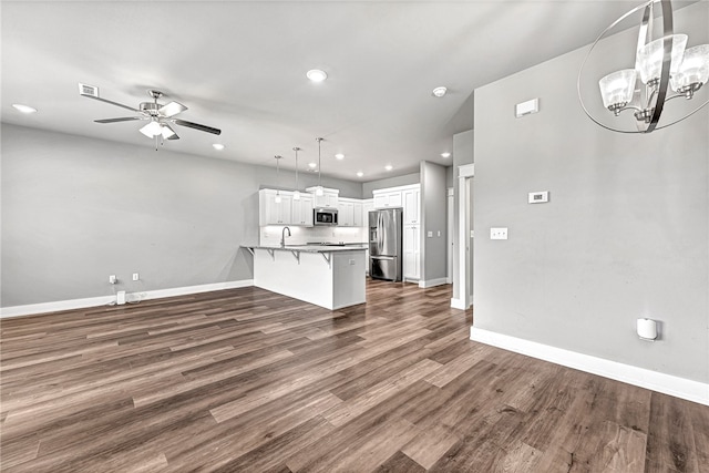 kitchen with dark wood-type flooring, kitchen peninsula, stainless steel appliances, a kitchen bar, and white cabinetry