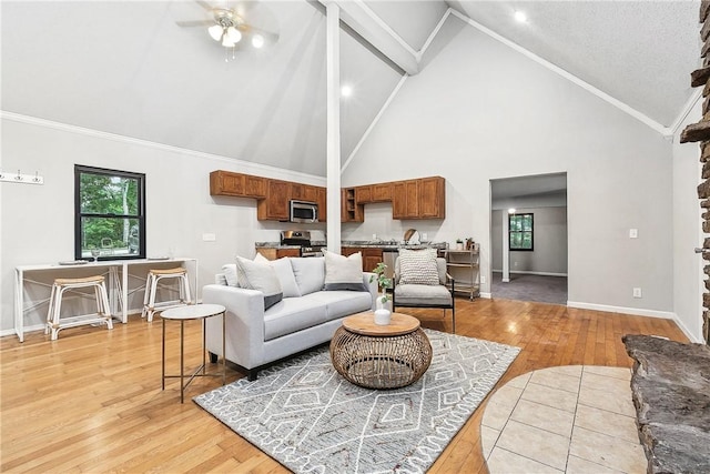 living room with ceiling fan, crown molding, high vaulted ceiling, and light wood-type flooring