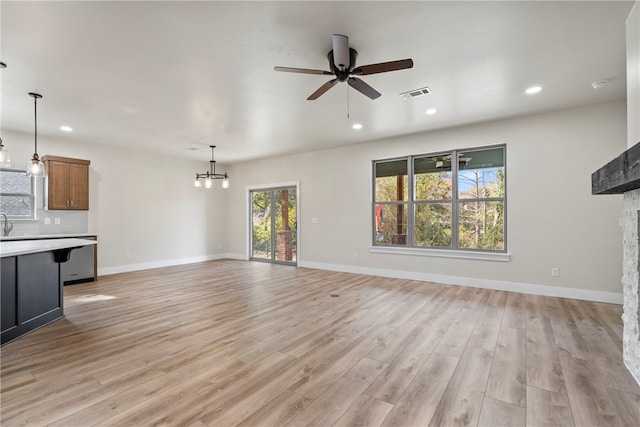 unfurnished living room featuring a fireplace, ceiling fan with notable chandelier, and light wood-type flooring