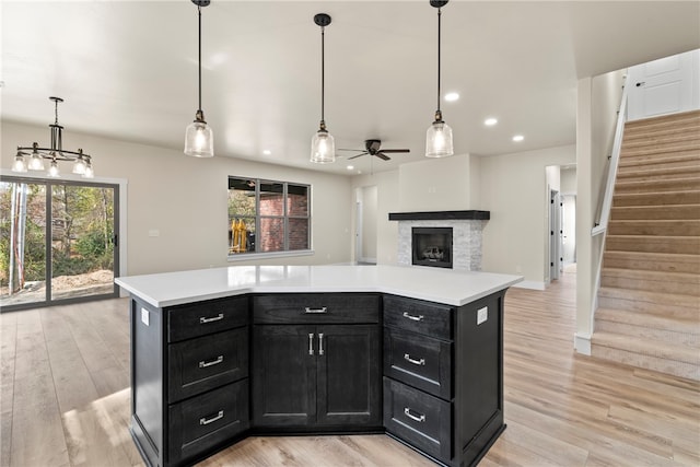 kitchen featuring a fireplace, pendant lighting, light hardwood / wood-style floors, ceiling fan, and a center island