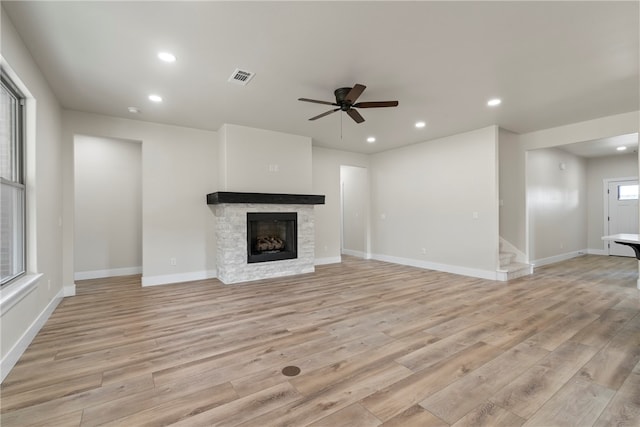 unfurnished living room featuring a stone fireplace, ceiling fan, and light hardwood / wood-style floors