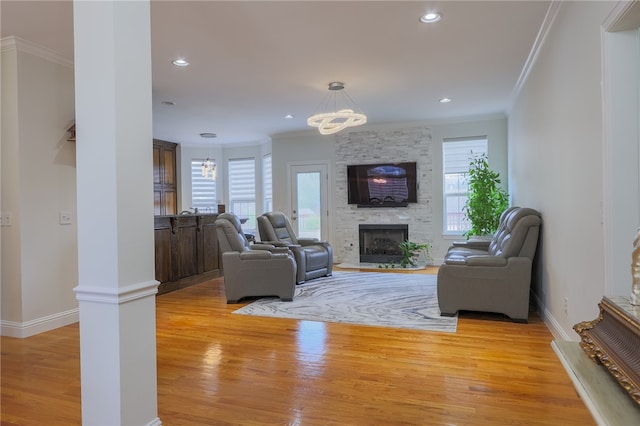 living room with ornamental molding, a wealth of natural light, light hardwood / wood-style floors, and a stone fireplace