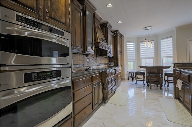 kitchen with decorative backsplash, dark brown cabinetry, stainless steel double oven, ornamental molding, and decorative light fixtures