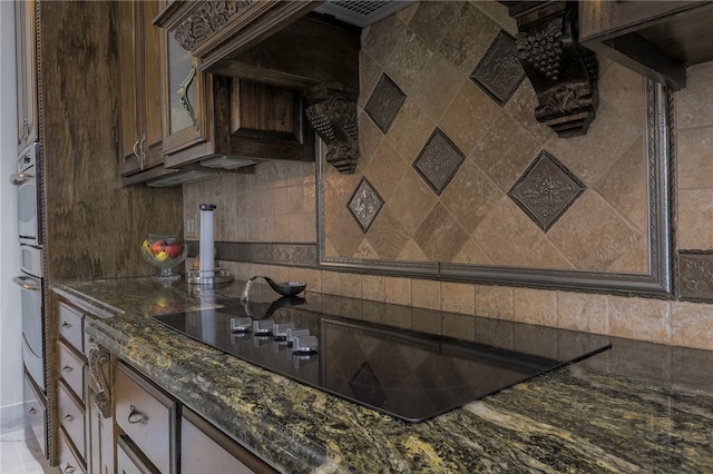 kitchen featuring black electric stovetop, tasteful backsplash, white oven, dark brown cabinets, and dark stone countertops