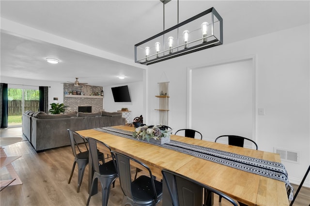 dining area featuring ceiling fan with notable chandelier, hardwood / wood-style flooring, and a fireplace