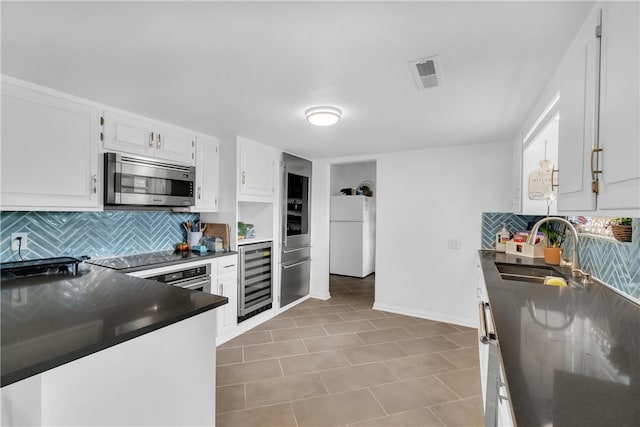 kitchen featuring white fridge, beverage cooler, backsplash, sink, and white cabinetry