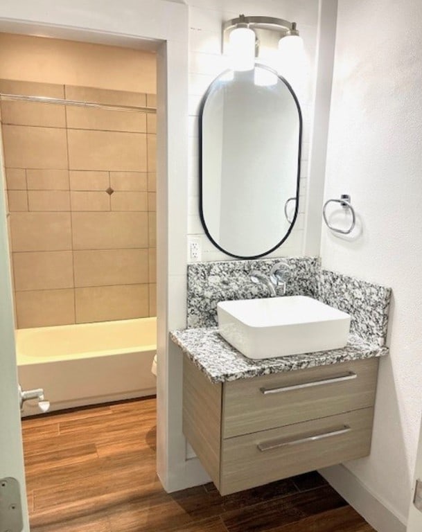 bathroom with washtub / shower combination, wood finished floors, vanity, and baseboards