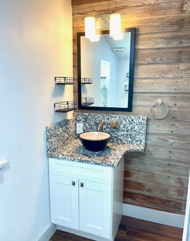 bathroom featuring baseboards, wood finished floors, vanity, and wooden walls