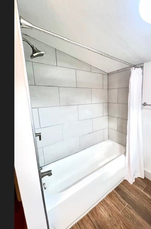 bathroom featuring hardwood / wood-style floors, a textured ceiling, shower / bathtub combination with curtain, and lofted ceiling