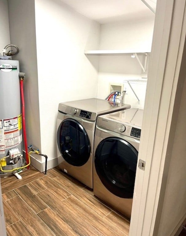 clothes washing area featuring gas water heater, washing machine and clothes dryer, wood tiled floor, laundry area, and baseboards