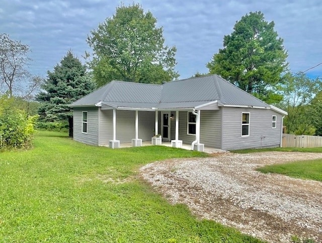 view of front of house featuring driveway, metal roof, fence, and a front lawn