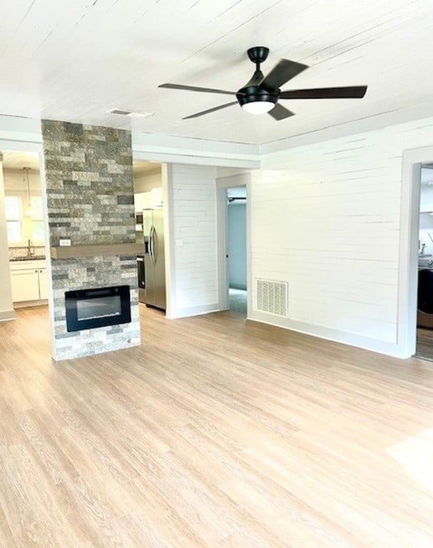 unfurnished living room featuring a stone fireplace, ceiling fan, sink, and light wood-type flooring