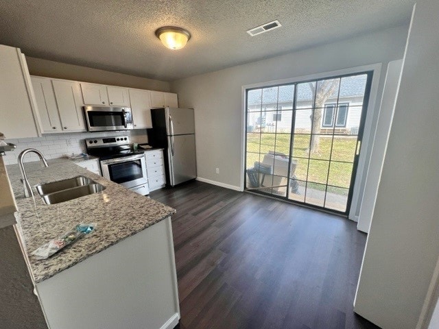 kitchen with appliances with stainless steel finishes, light stone countertops, dark hardwood / wood-style flooring, white cabinetry, and sink