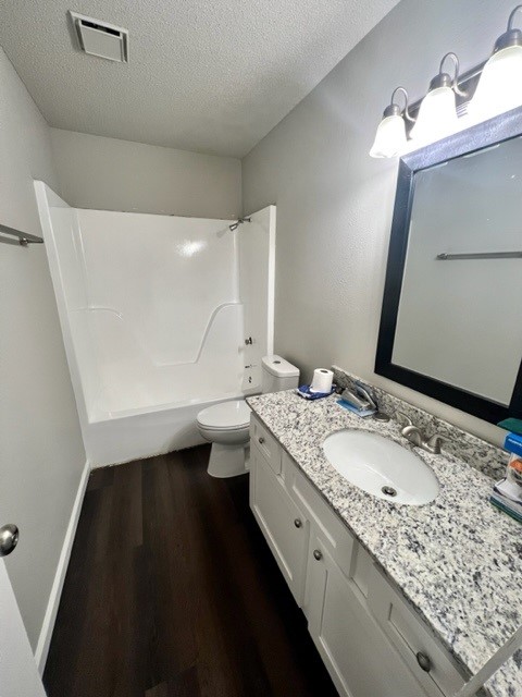 full bathroom with a textured ceiling, vanity, wood-type flooring, toilet, and tub / shower combination