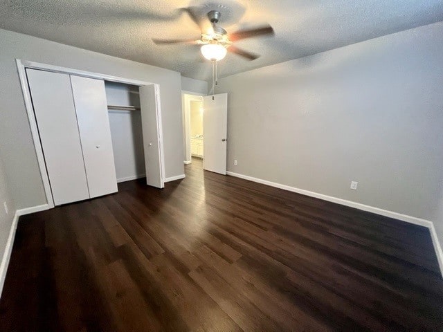 unfurnished bedroom with dark wood-type flooring, a textured ceiling, ceiling fan, and a closet