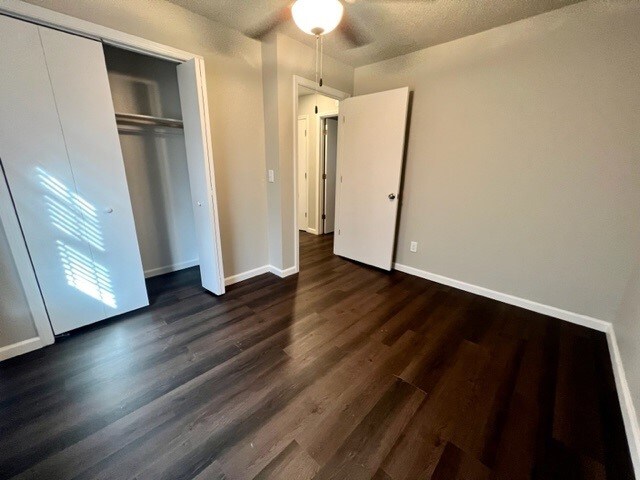 unfurnished bedroom featuring a closet, ceiling fan, dark hardwood / wood-style floors, and a textured ceiling