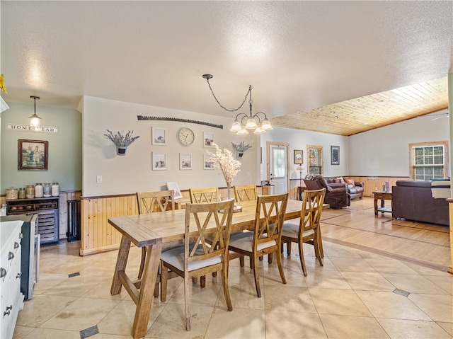 dining space with an inviting chandelier, a textured ceiling, wooden walls, and plenty of natural light