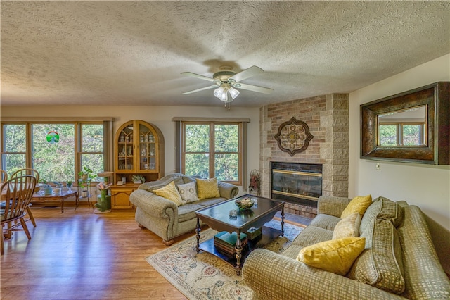 living room featuring light wood-type flooring, a healthy amount of sunlight, a textured ceiling, and a large fireplace