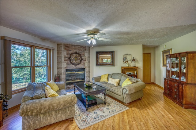 living room with ceiling fan, a textured ceiling, light hardwood / wood-style flooring, and a fireplace