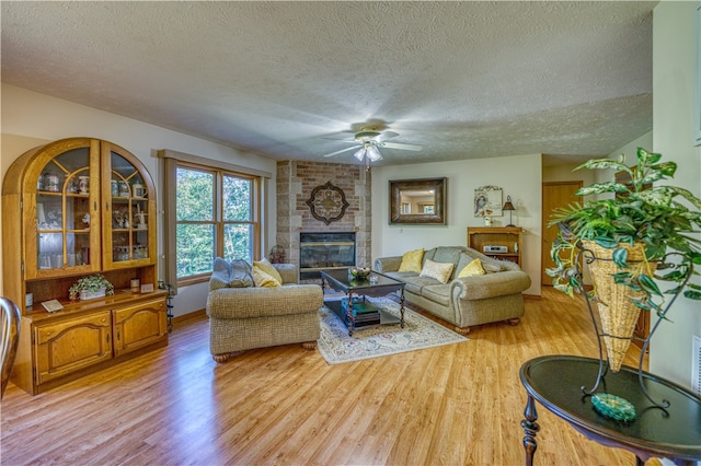 living room with a brick fireplace, light hardwood / wood-style floors, a textured ceiling, and ceiling fan