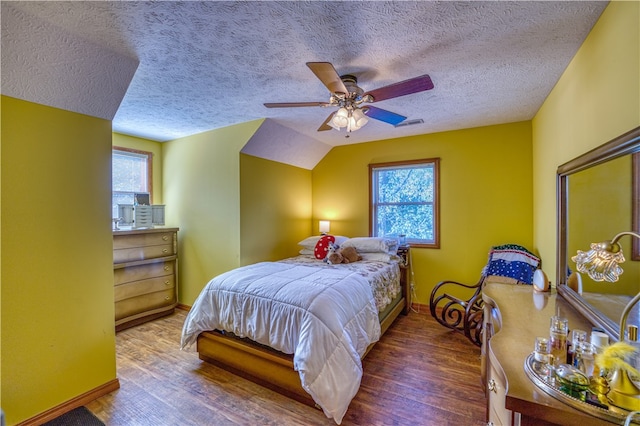 bedroom with a textured ceiling, ceiling fan, multiple windows, and dark hardwood / wood-style flooring