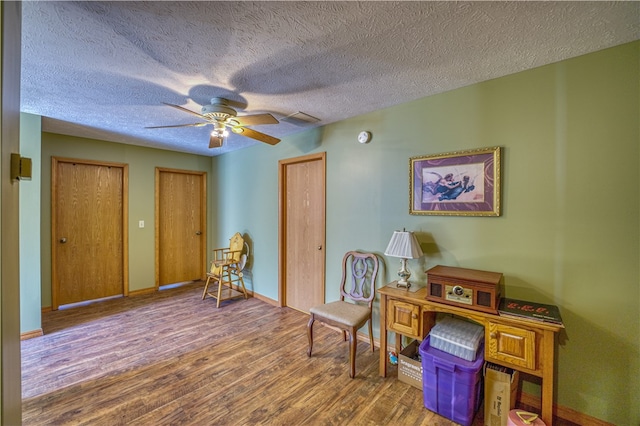 living area featuring wood-type flooring, a textured ceiling, and ceiling fan