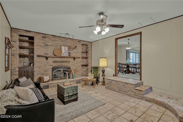 living room featuring a brick fireplace, wooden walls, a textured ceiling, and ceiling fan