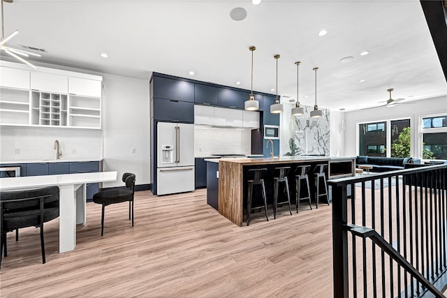 kitchen with light hardwood / wood-style flooring, an island with sink, high end white fridge, decorative backsplash, and ceiling fan