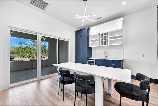 kitchen with pendant lighting, light hardwood / wood-style flooring, backsplash, a chandelier, and blue cabinets