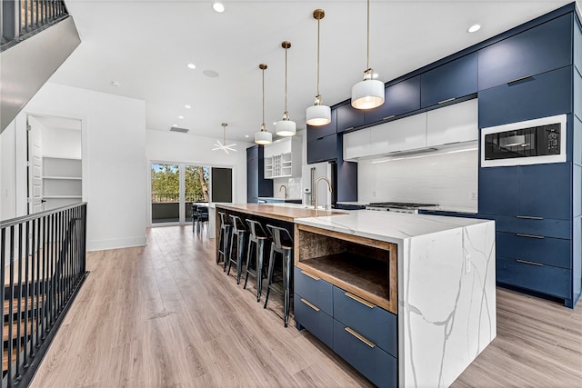 kitchen with light stone countertops, a spacious island, blue cabinetry, light hardwood / wood-style floors, and hanging light fixtures