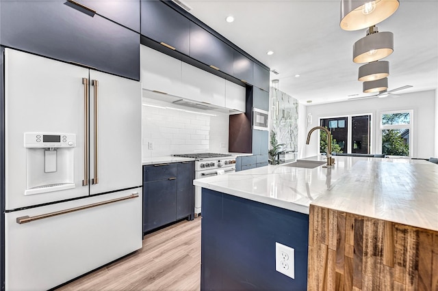 kitchen featuring high quality appliances, decorative light fixtures, sink, ceiling fan, and light stone countertops