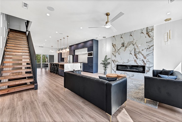 living room featuring light wood-type flooring, ceiling fan, and a high end fireplace