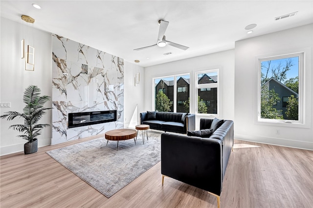 living room with a high end fireplace, light wood-type flooring, a healthy amount of sunlight, and ceiling fan