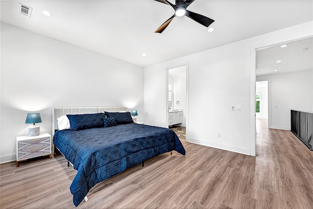 bedroom with light wood-type flooring, ceiling fan, and ensuite bath