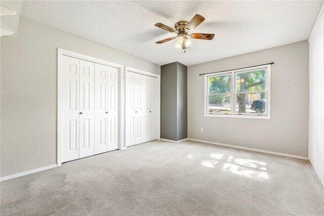 unfurnished bedroom with two closets, ceiling fan, light colored carpet, and a textured ceiling