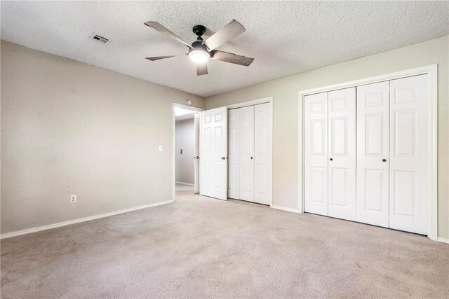 unfurnished bedroom featuring a textured ceiling, light colored carpet, ceiling fan, and multiple closets