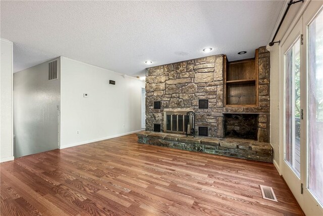 unfurnished living room featuring hardwood / wood-style flooring, a textured ceiling, and a stone fireplace